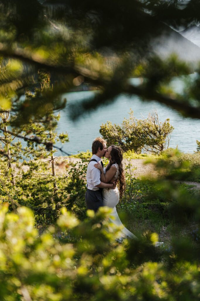 Bride and groom kiss while framed by the trees at Sun Point in Glacier National Park.