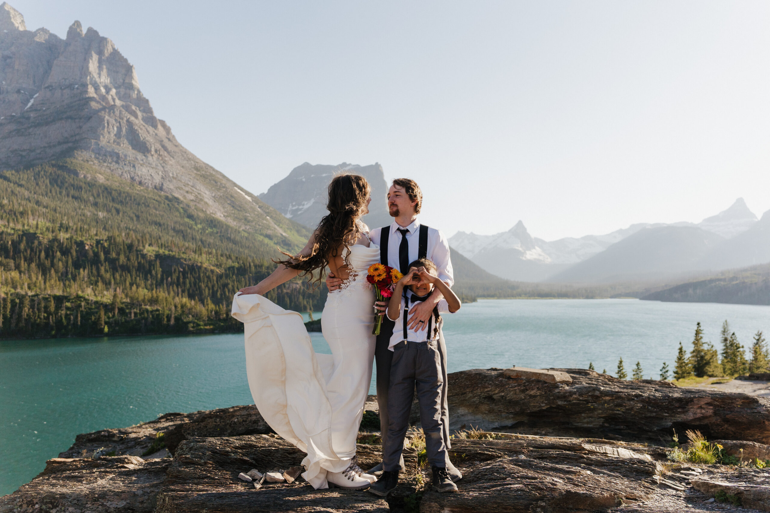 couple poses with son in the wind of Sun Point after eloping at Glacier National Park.