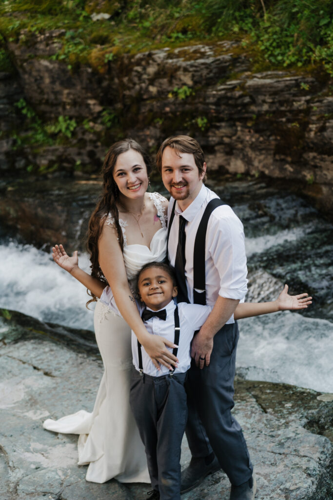 The family posing by the waterfall after eloping at Sun Point in Glacier National Park.