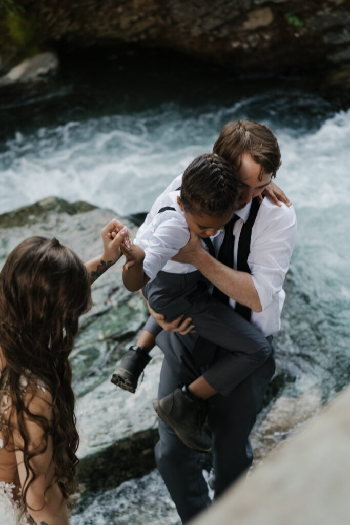 The family stepping over the waterfall after eloping at Sun Point in Glacier National Park.