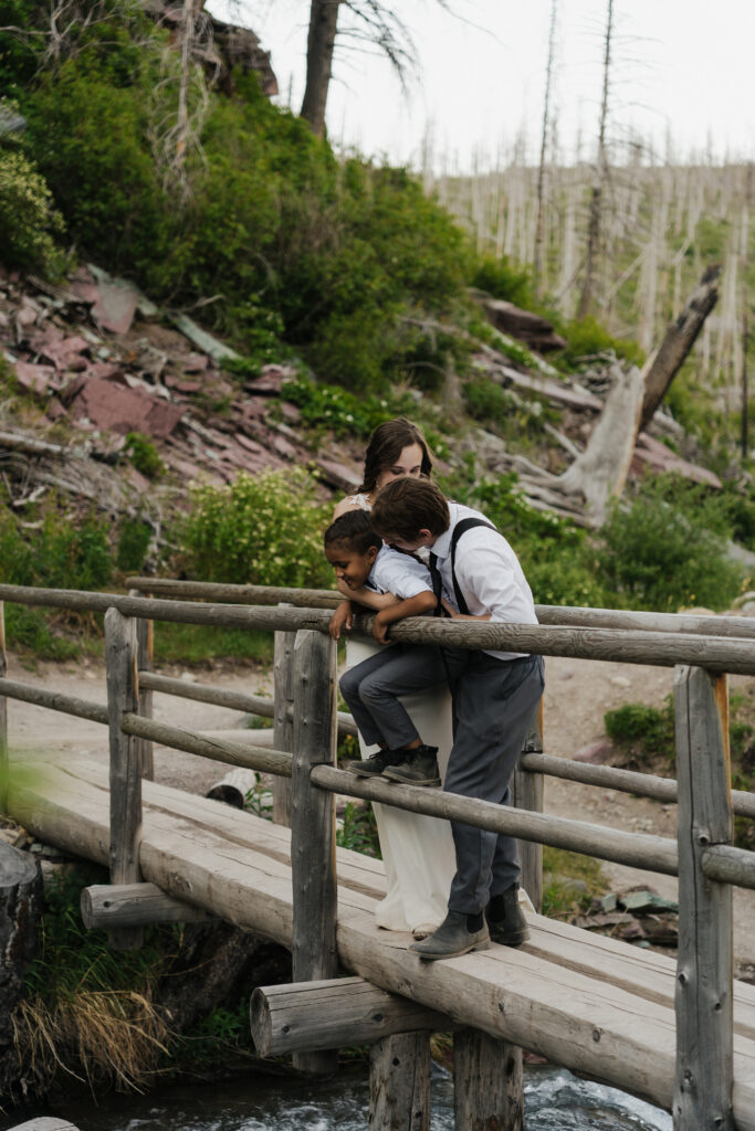 The family stands on a bridge and looks at the water below.