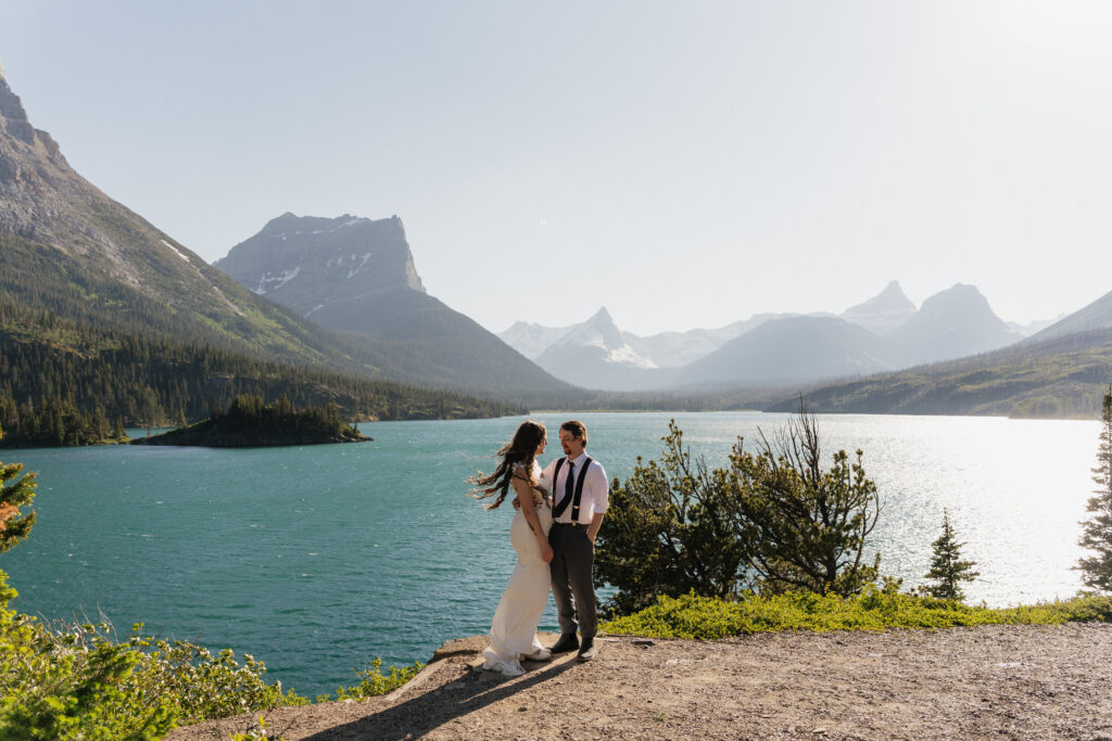 Bree and Will standing together eloping at Sun Point in Glacier National Park, holding hands with mountain peaks behind them.
