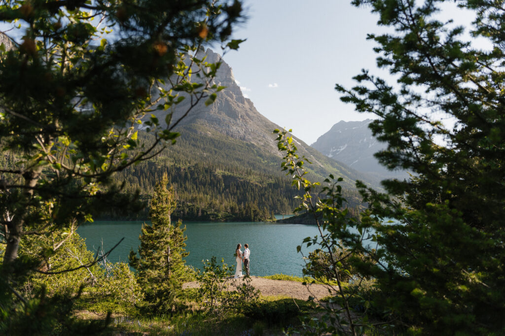 Bride and Groom framed by trees while they exchange vows at Glacier National Park.