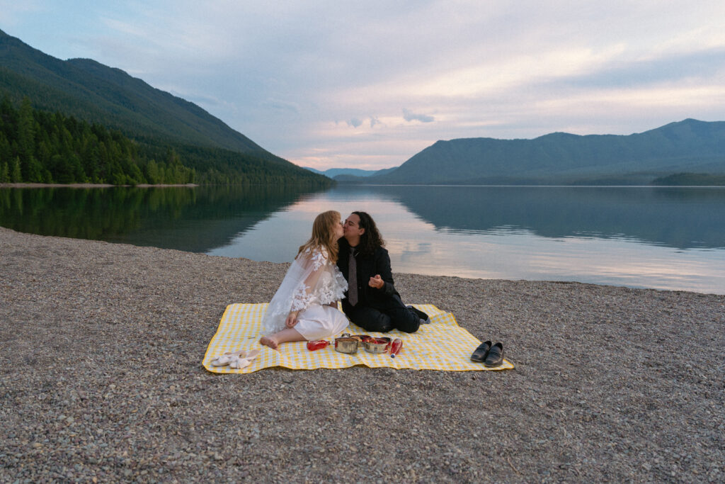 Couple kisses on a picnic blanket over Lake McDonald.