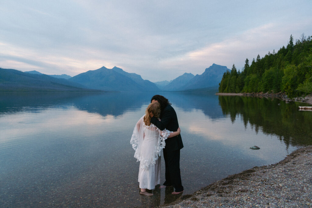 Bride and groom kiss in Lake McDonald after elopement in Glacier National Park.