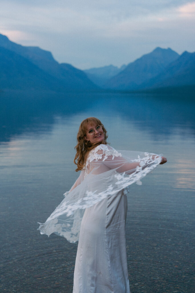Bride spins lace cape in Lake McDonald after elopement in Glacier National Park.