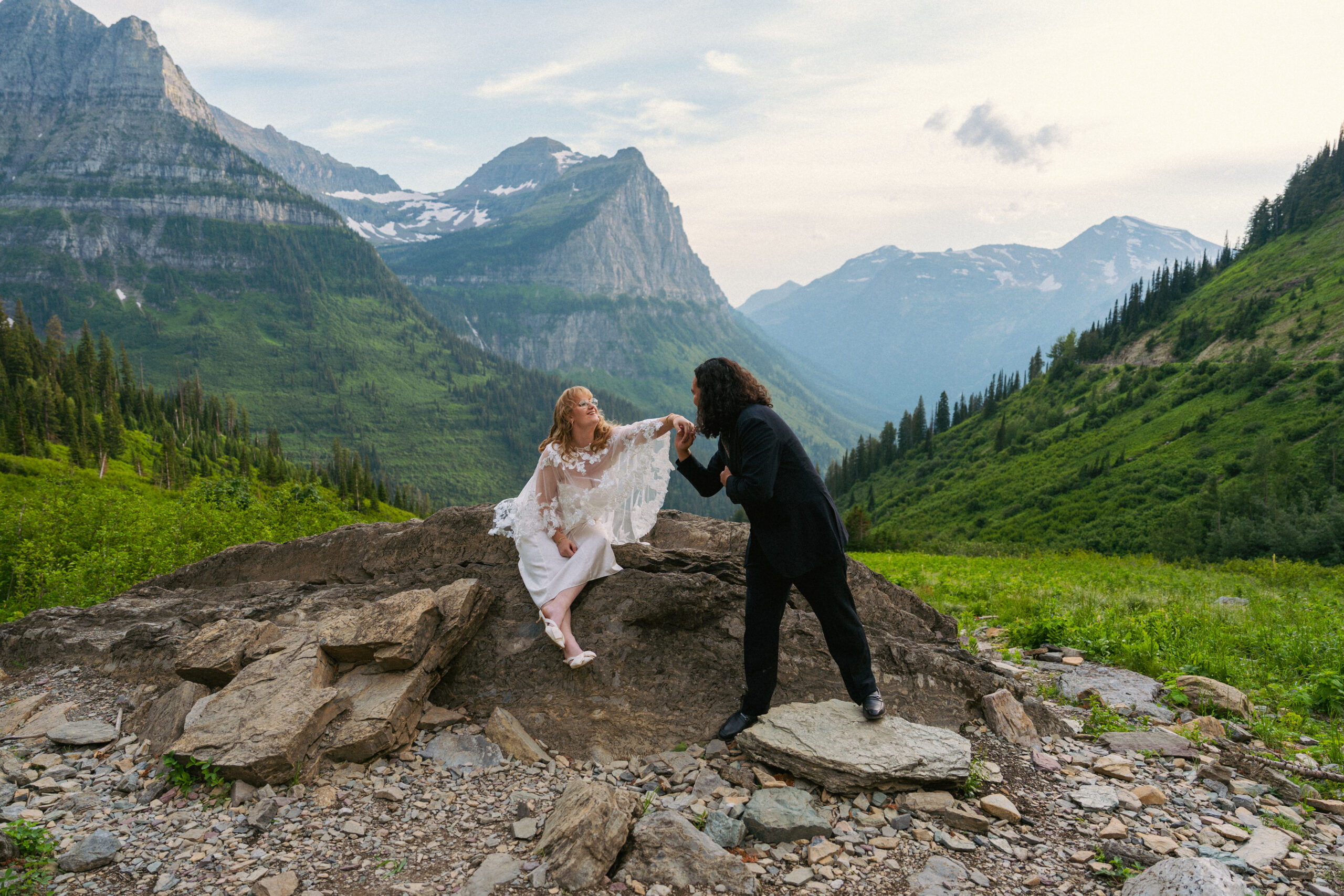 Eddy leaning in to kiss Nina's had with huge mountain backdrop in Glacier National Park.