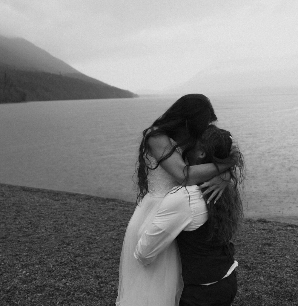Couple embracing in black and white overlooking a foggy Lake McDonand in Glacier National Park