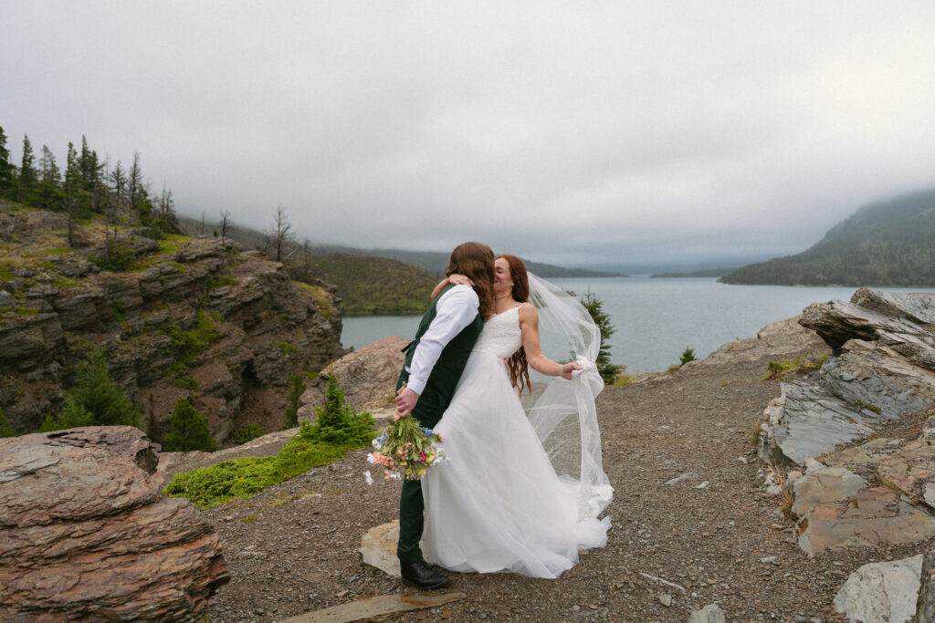 Groom dips bride while holding veil in the wind at Glacier National Park