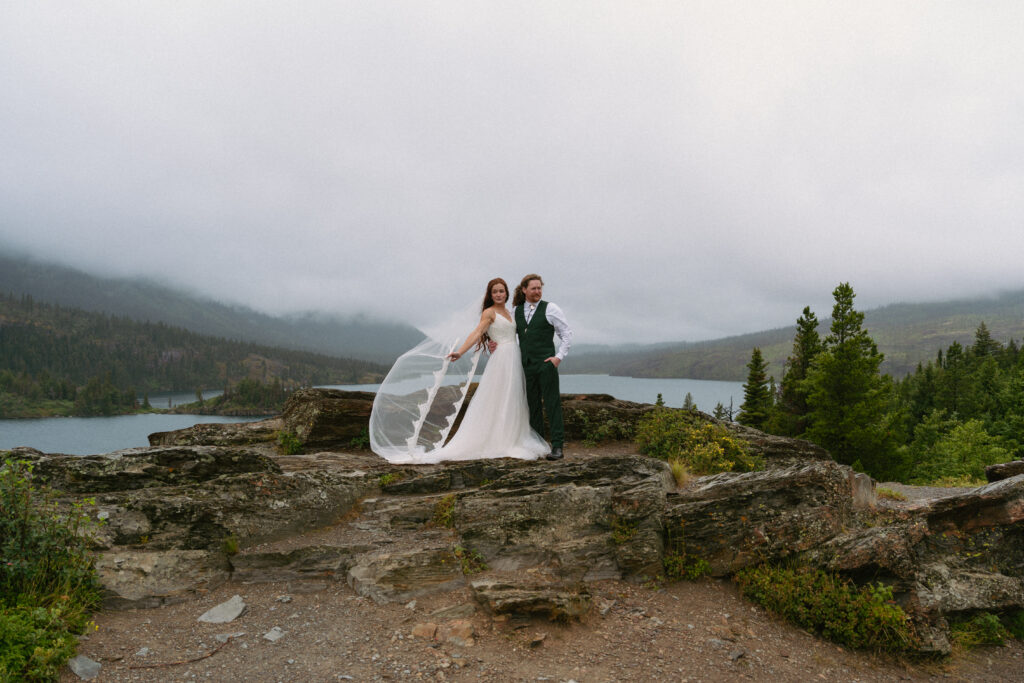 Couple posing in the wind on top of an overlook at Glacier National Park