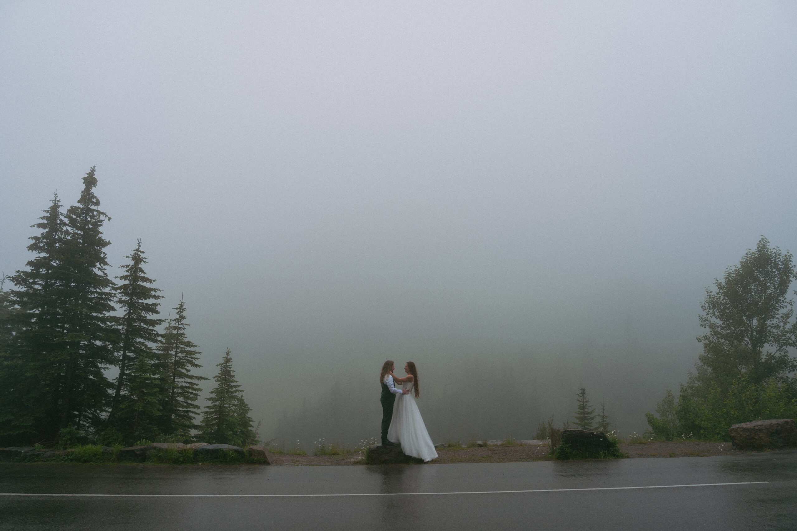 Couple poses on a rock on Going to the Sun Road with very moody clouds.