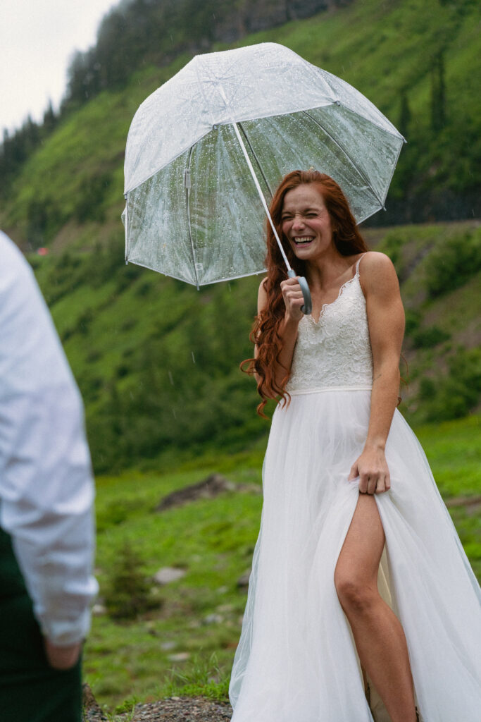 Bride laughing under an umbrella at a foggy spot on Going to the Sun Road at Glacier National Park