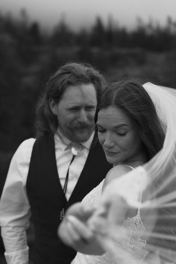 Close up of bride in grooms arms while holding veil in the wind at Glacier National Park