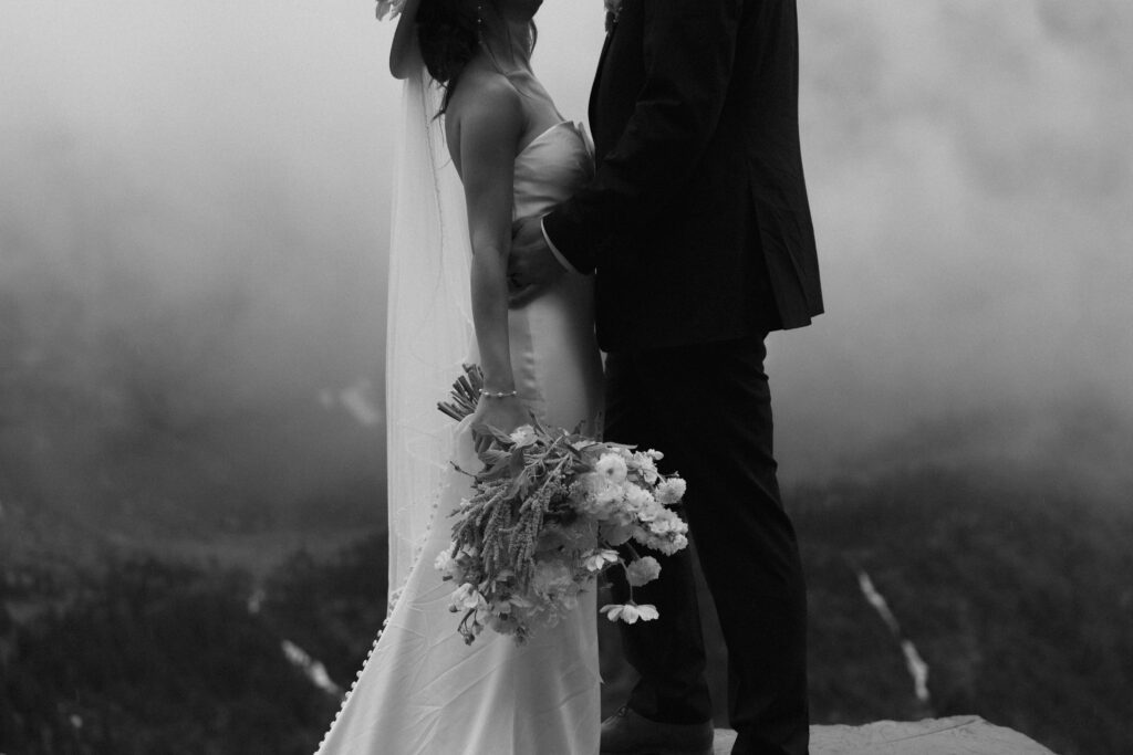 Black and white photo of a couple standing on a rock in Glacier National park.